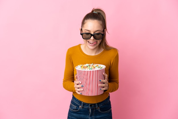 Young Lithuanian woman isolated on pink wall with 3d glasses and holding a big bucket of popcorns