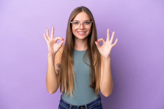Молодая литовская женщина, изолированная на фиолетовом фоне, показывает знак "ок" двумя руками