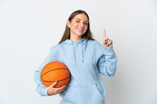 Молодая литовская женщина играет в баскетбол на белом фоне, показывая и поднимая палец в знак лучших