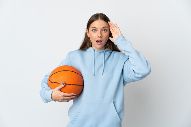 Молодая литовская женщина играет в баскетбол изолирована на белой стене с удивленным выражением лица