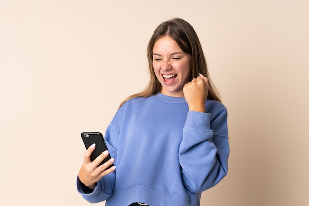 Young Lithuanian woman using mobile phone isolated on beige celebrating a victory