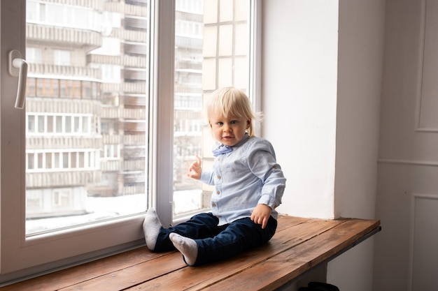 Young little child toddler boy sitting on window. Coronavirus theme. Stay at home.