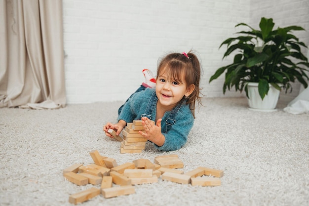 若いかわいい女の子は、木製のブロック、木のおもちゃの建設から家を建てます。子供たちはコピースペースで創造的な概念を遊んで学びます。