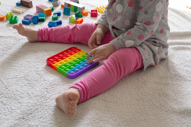 Young little girl sitting on rug at home and playing with new trendy toy pop it