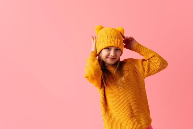 Young little girl wearing yellow sweater and hat isolated on pink background