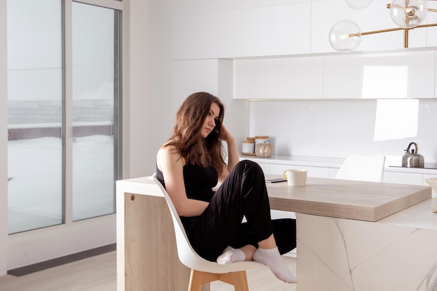 Young lonely brunette woman sitting in the kitchen and dreaming