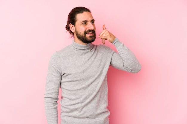 Young long hair man isolated on a pink showing a mobile phone call gesture with fingers.