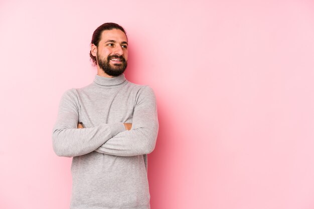 Young long hair man isolated on pink smiling confident with crossed arms.