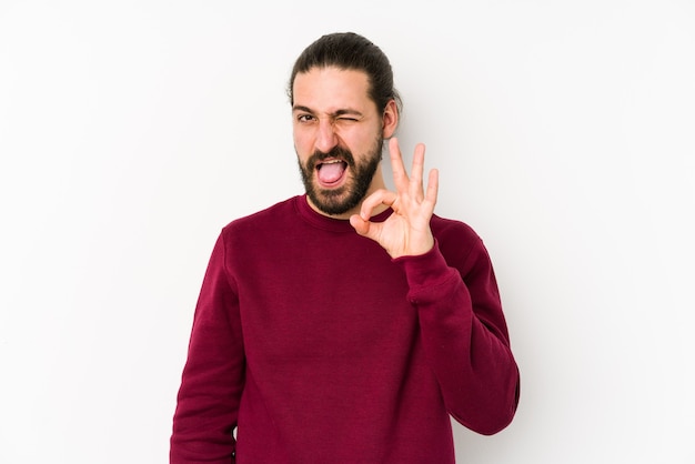 Young long hair man isolated on a white surface winks an eye and holds an okay gesture with hand.