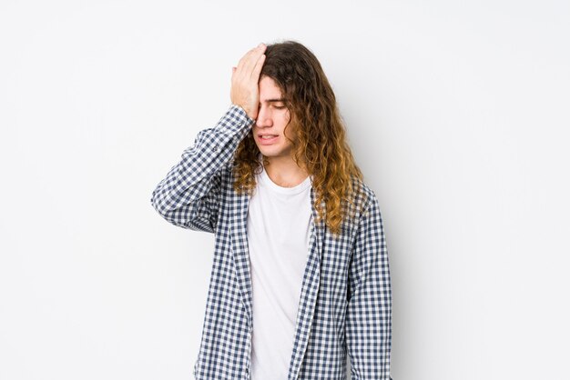 Young long hair man posing isolated forgetting something, slapping forehead with palm and closing eyes.