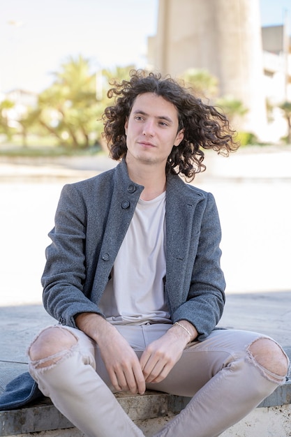 Young long hair man sitting on the pavement on the street