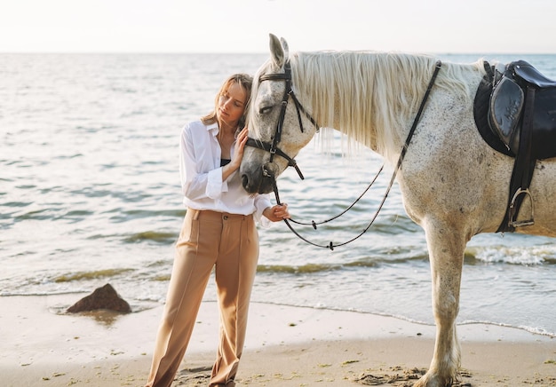 Young long hair woman in white shirt with white horse on seascape background