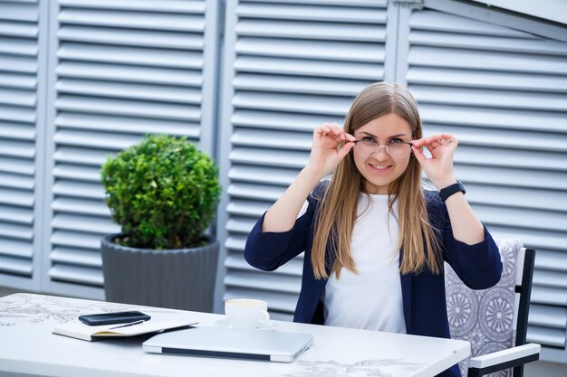 Young long-haired woman working with a laptop, sitting on an outdoor terrace in a cafe. Business development concept, girl in the lunch break working over a cup of coffee