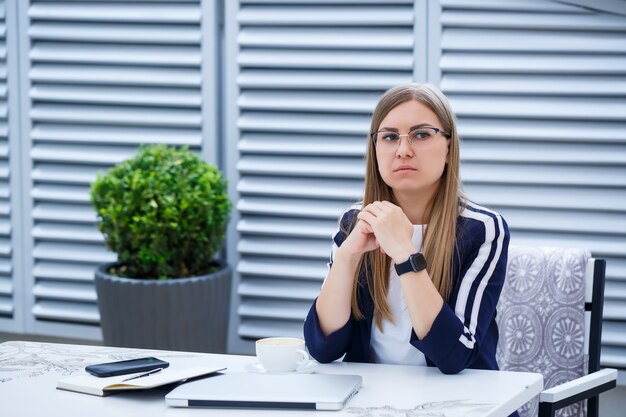 Foto giovane donna dai capelli lunghi che lavora con un computer portatile, seduta su una terrazza all'aperto in un caffè. concetto di sviluppo del business, ragazza in pausa pranzo che lavora davanti a una tazza di caffè