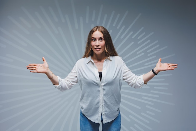 Foto giovane donna dai capelli lunghi in jeans e una camicia bianca su sfondo chiaro emozioni sul volto di una donna