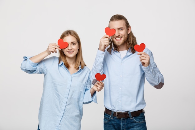 young in love couple holding red hearts over eyes on white background