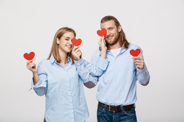 young in love couple holding red hearts over eyes on white background