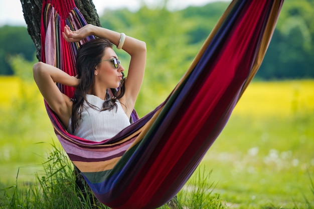 Young lovely brunette in sunglasses is lies in a hammock against the background of the field. Close-up.