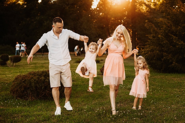 Young lovely family having fun outdoor against sunset. Two little daughters playing with her mother and father.