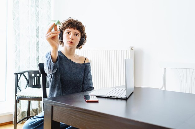 Young lovely girl teenager headphones playing with paper plane while sitting at table