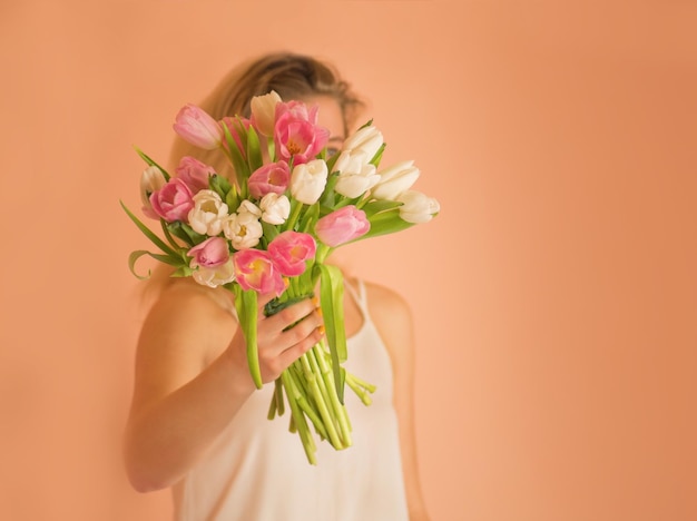 カラフルな新鮮な花のチューリップと白いドレスの若い素敵な女の子