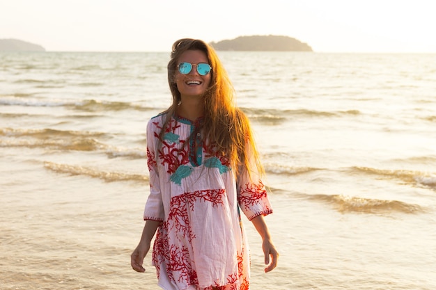 Young lovely woman wearing beautiful dress  is walking by the sea shore during sunset