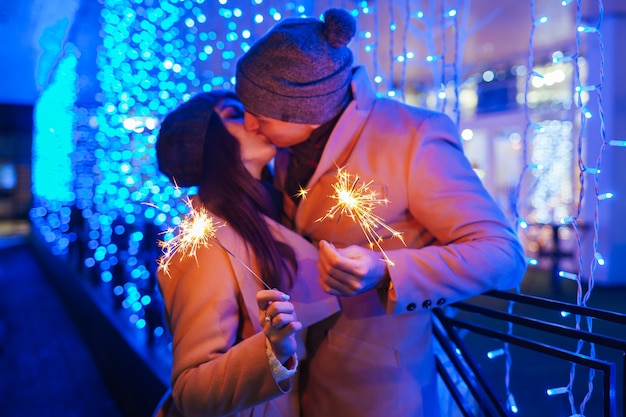 休日のイルミネーションで線香花火を燃やす若い愛情のあるカップル。クリスマスと新年のコンセプト