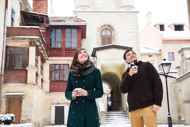 Молодая любящая пара, одетая в повседневный стиль, гуляет по старому городу зимой и пьет горячий чай и кофе