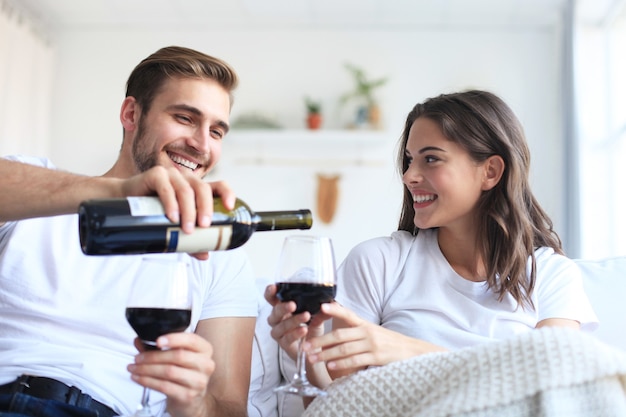 Giovani coppie amorose che bevono un bicchiere di vino rosso nel loro soggiorno.