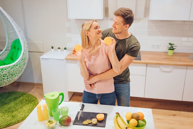 Young loving couple has fun with organic orange while cooking fresh fruits in white kitchen