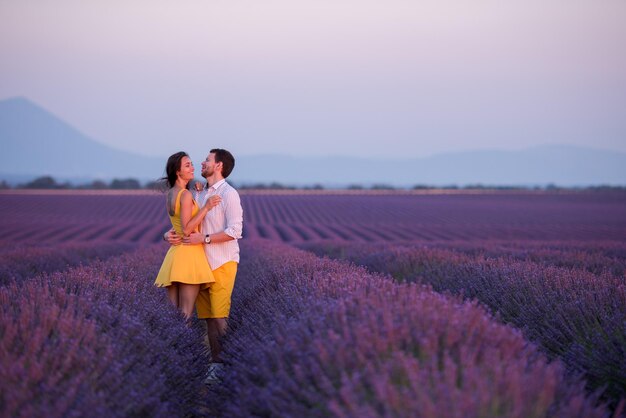 夕暮れの紫色のラベンダーの花畑でハグとキスをするロマンチックな時間を過ごす若い愛情のあるカップル
