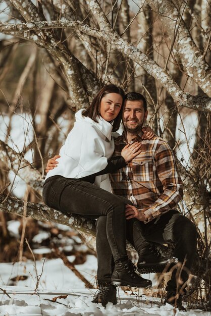 Young loving couple sitting on a trunk in the forest Cold winter clothing Love story Selective focus
