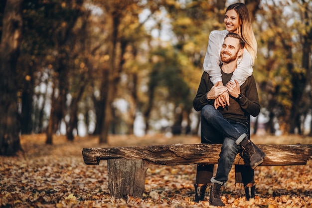 A young loving couple sitting on a wooden bench in the forest.