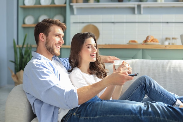 Young loving couple on sofa at home watching tv and laughing.