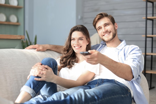 Young loving couple on sofa at home watching tv and laughing.