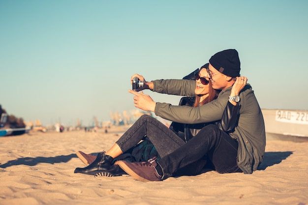 A young loving couple spends fun time by the sea and makes selfies. Man and woman have spring clothes