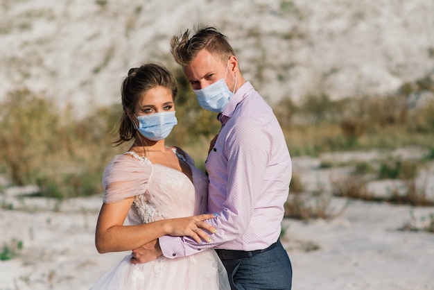 Young loving couple walking in medical masks in the park during quarantine on their wedding day.