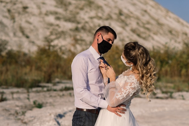 Young loving couple walking in medical masks in the park during quarantine on their wedding day.