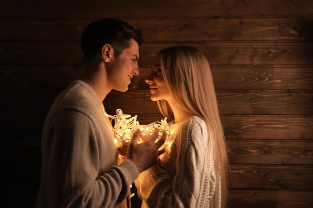 Young loving couple with fairy lights on wooden background