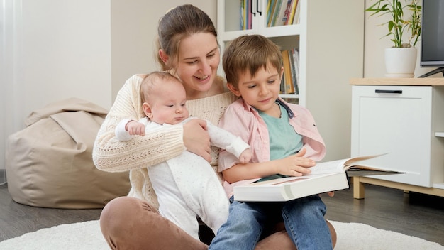 Foto giovane madre amorevole seduta con i suoi figli in soggiorno e leggendo un libro di fiabe genitori figli