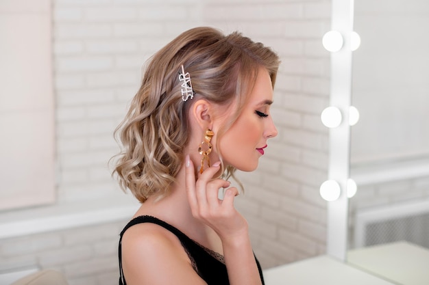 Young luxury woman with blonde hairstyle and makeup looking at the mirror in hairdressing salon