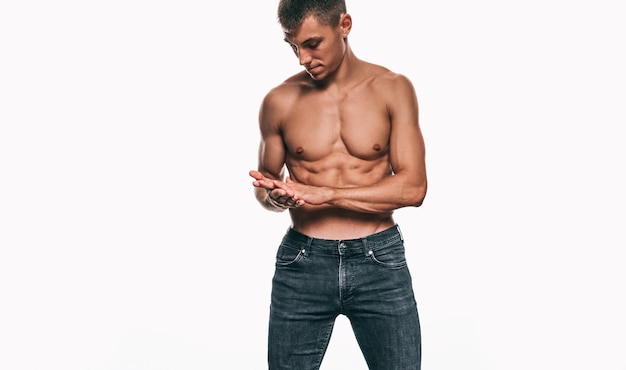 Young macho male model in jeans showing his sexy body isolated on a white background Shirtless bodybuilder man with sexy abdomen posing over white wall Health sport and people concept