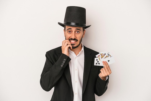 Young magician man holding a magic card isolated on white background biting fingernails nervous and very anxious