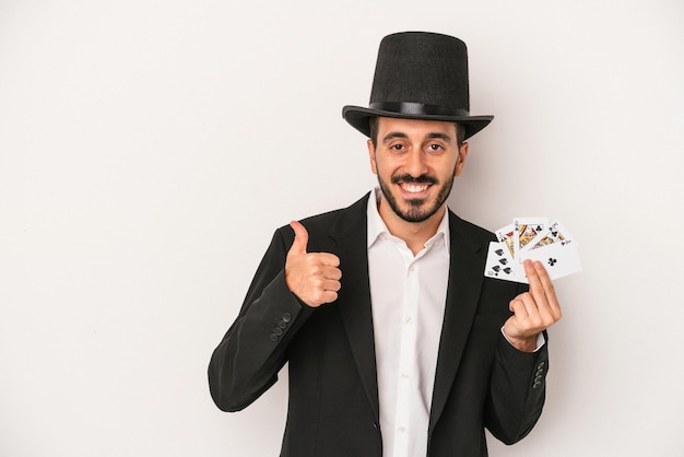 Young magician man holding a magic card isolated on white background smiling and raising thumb up