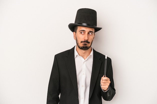 Young magician man holding wand isolated on white background confused, feels doubtful and unsure.