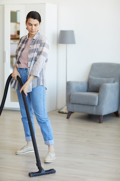 Young maid cleaning the house using vacuum cleaner