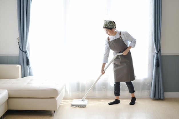 a young maid cleaning the house with a mop there is a kitchen backdrop