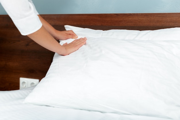 Young maid making bed in hotel room