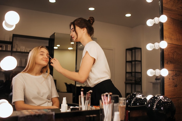 Photo young makeup artist put makeup of young woman's face