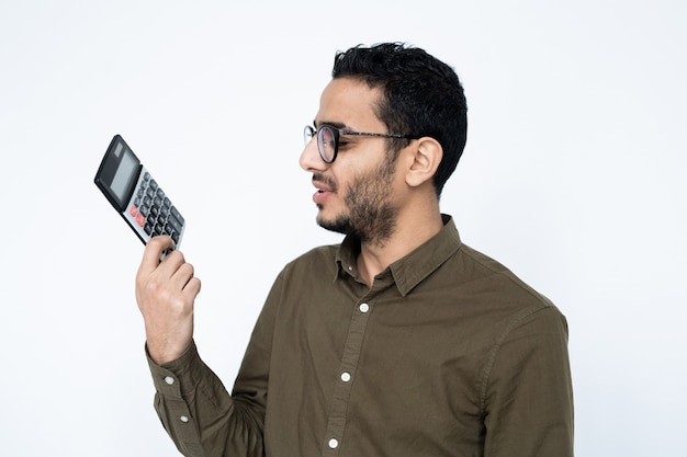 Young male accountant or student in eyeglasses looking at calculator in his hand with dissatisfied expression
